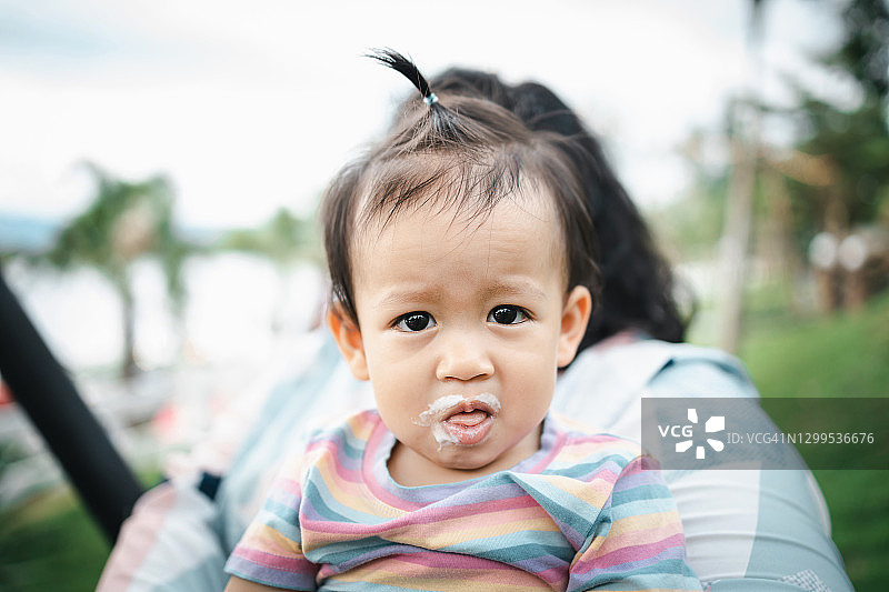坐在母亲腿上，嘴边有冰淇淋的可爱女婴图片素材