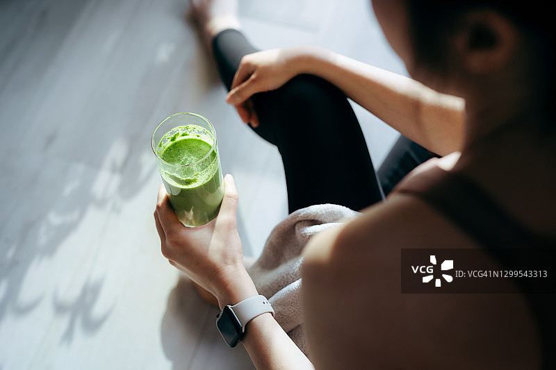年轻亚洲运动女性在家锻炼后，享用健康绿色果汁图片素材