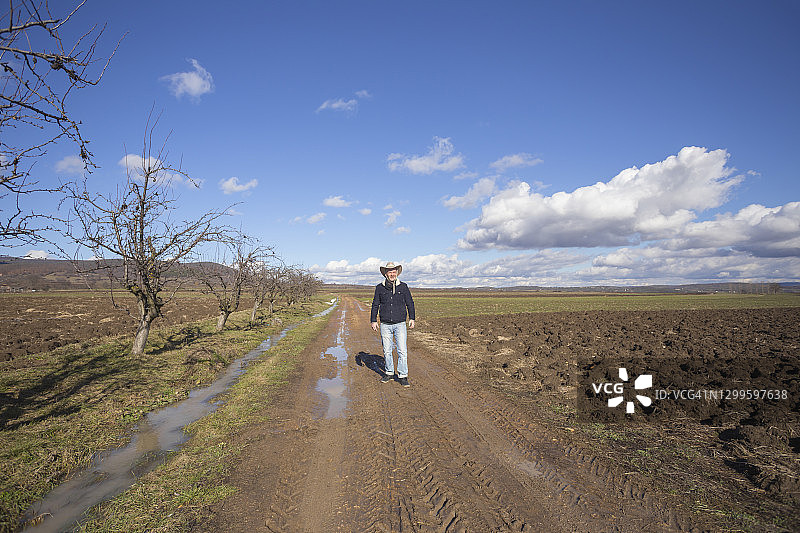戴牛仔帽的成熟农民站在农田泥土路上图片素材