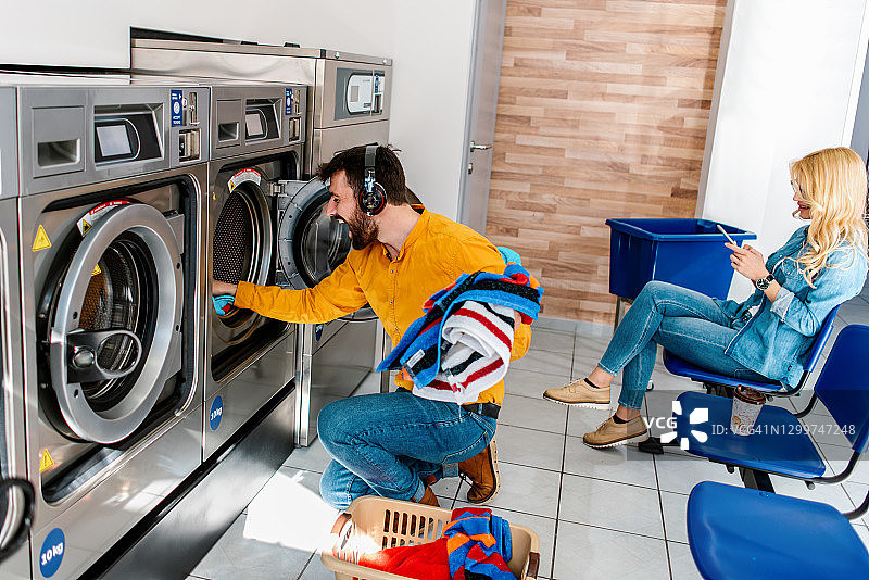 年轻快乐的夫妇在自助洗衣店一起洗衣服。图片素材