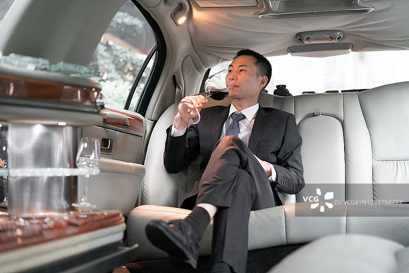在豪华轿车里喝酒的亚洲商人图片素材