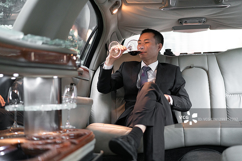 在豪华轿车里喝酒的亚洲商人图片素材