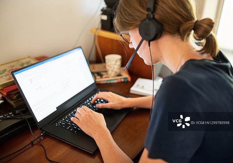 戴着耳机在家用笔记本电脑工作的年轻女人图片素材