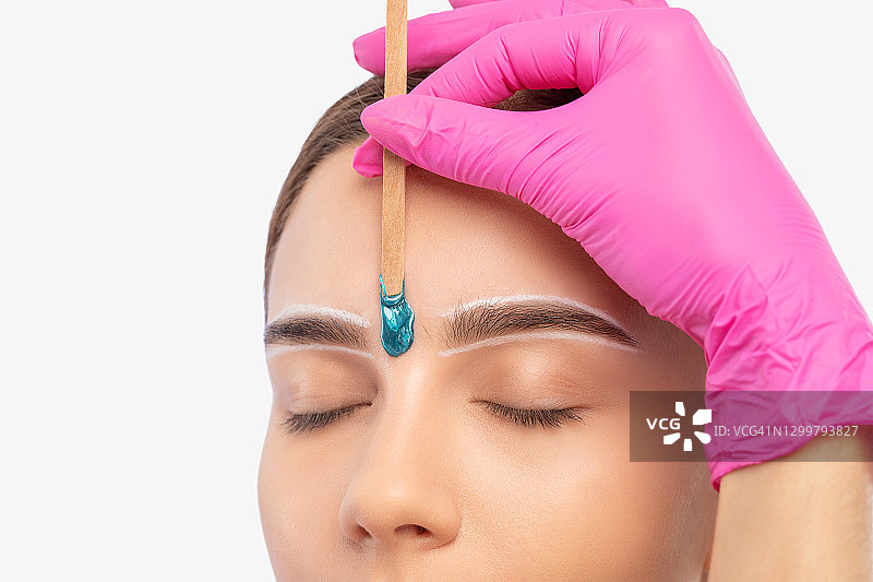 化妆师进行面部毛发去除程序，蓝眼睛美女正在进行眉毛的永久化妆。专业化妆。图片素材