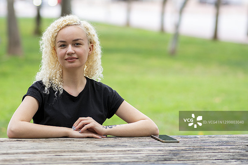 坐在公园长椅上享受户外阳光的年轻微笑女人图片素材