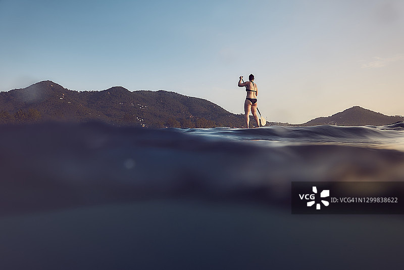 女子在热带海域日落时划桨板图片素材