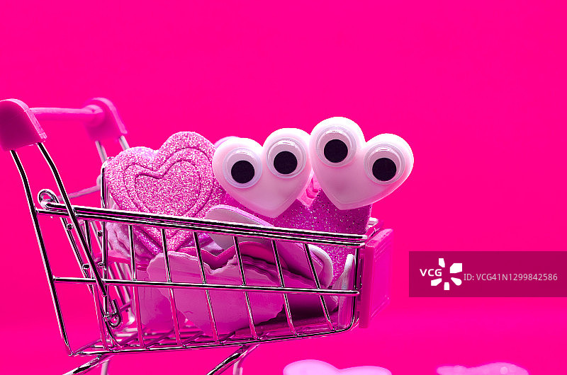 情人节：粉色背景上的卡通眼睛购物车和爱心图片素材