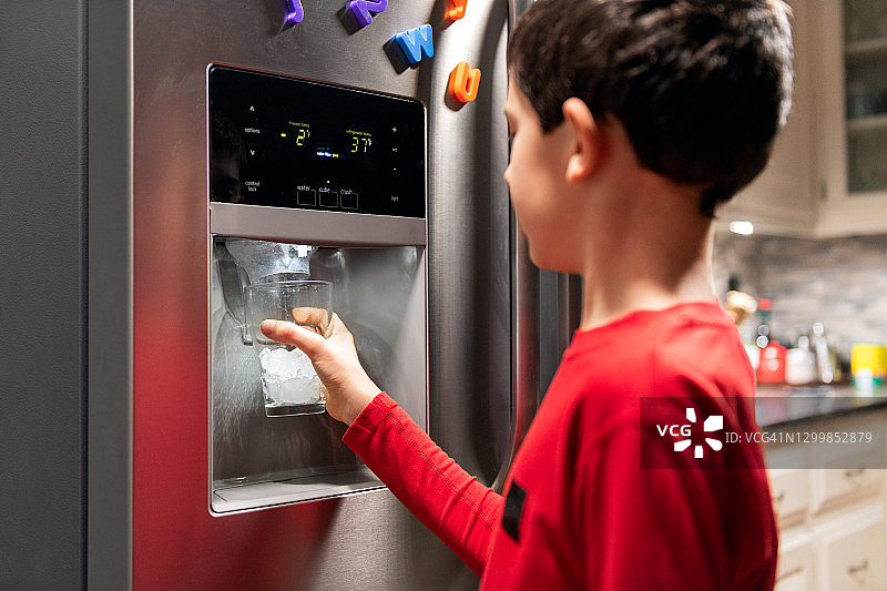 男孩从冰箱制冰机里取冰块倒入杯中图片素材