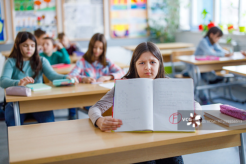 在小学展示不及格考卷的不开心女孩图片素材