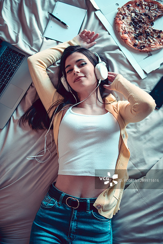 美女在床上放松，吃比萨，用笔记本电脑听音乐图片素材