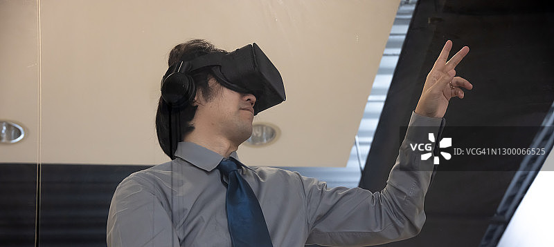 亚洲男人戴VR眼镜在办公室做手势。图片素材