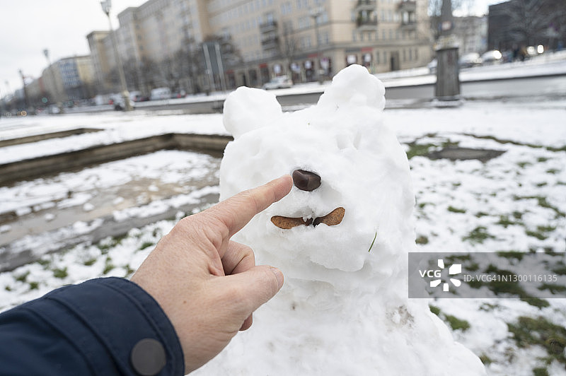 在德国柏林，男人用食指指着熊形雪人的鼻子图片素材
