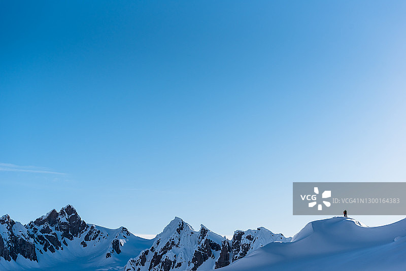 滑雪登山者攀登高耸山脉下的山脊线图片素材