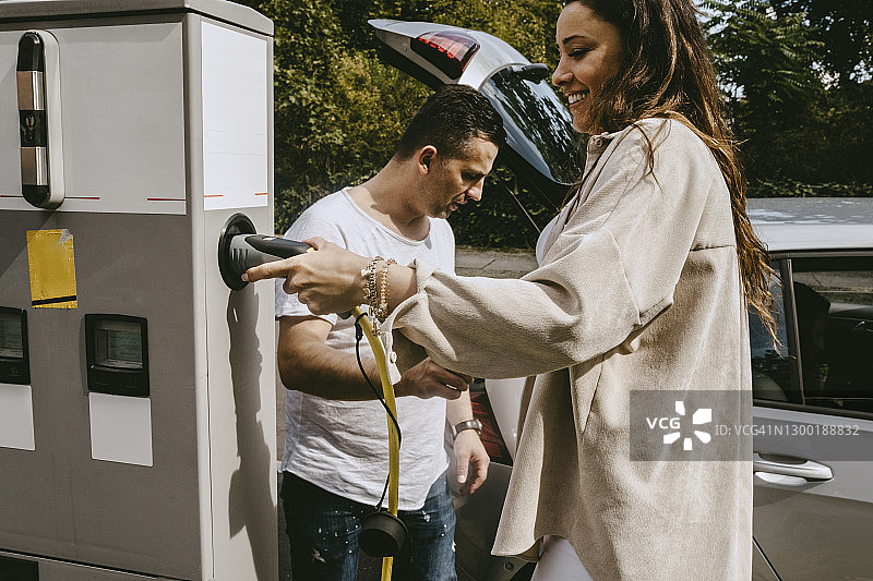 微笑的母亲拿着插头站在充电站父亲旁边图片素材