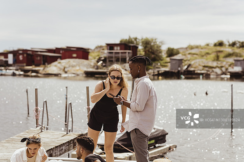 夏季假期，朋友们在港口窥视男人手机的女人图片素材