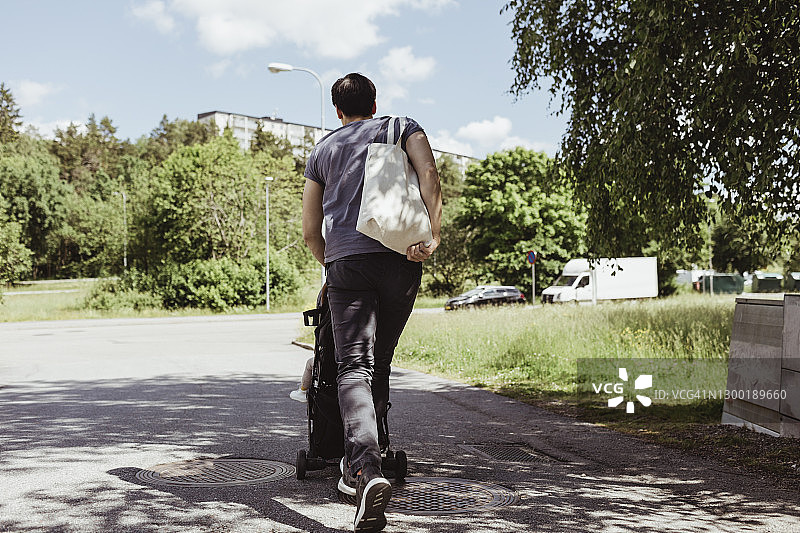 父亲在晴朗的一天推着婴儿车里的男婴在路上行走图片素材