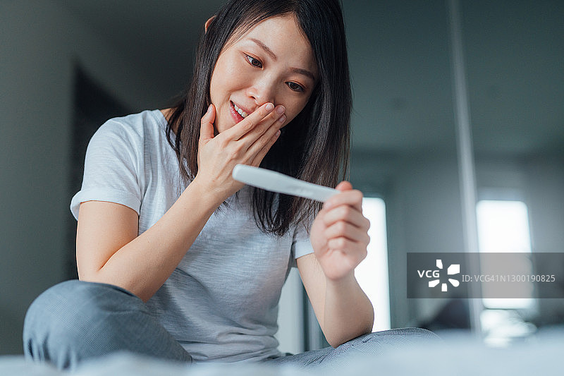 年轻女子在卧室里拿着验孕棒，看起来很高兴图片素材