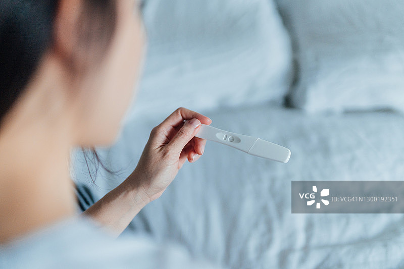 女子在卧室手持验孕棒的后视图图片素材