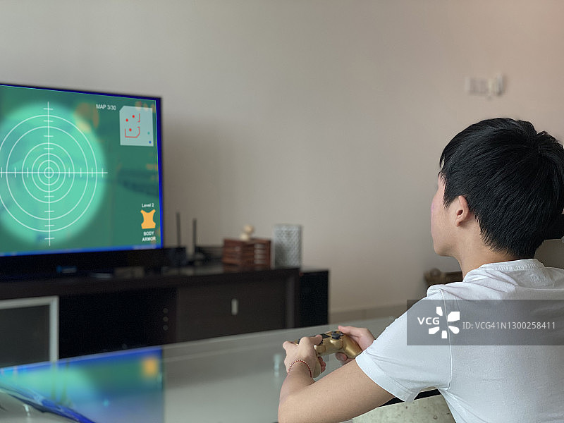 年轻男性游戏玩家在客厅使用游戏机控制器玩LED电视上的视频游戏图片素材
