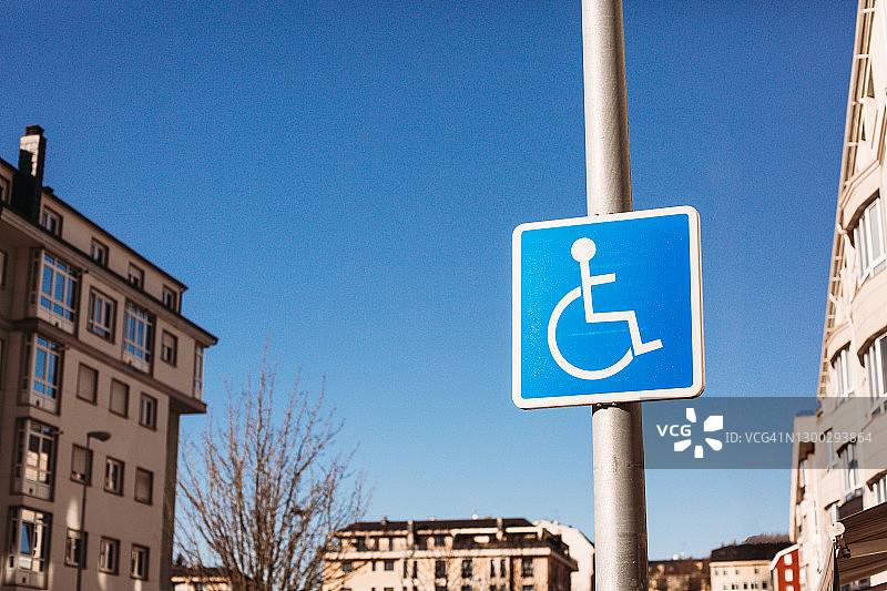 城市里建筑物背景下的灯柱上的残疾人停车标志图片素材