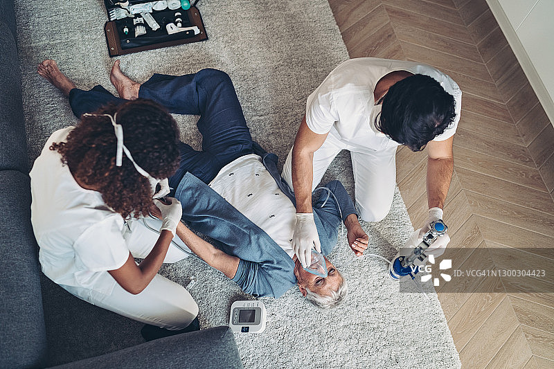 医生检查并吸入时，无助的老年妇女躺在地板上图片素材