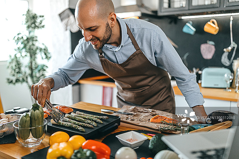 年轻男人在电烤架上烤三文鱼排和芦笋图片素材