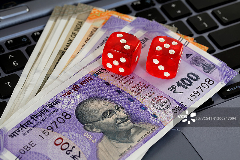 笔记本电脑键盘上的红色骰子和印度货币钞票图片素材