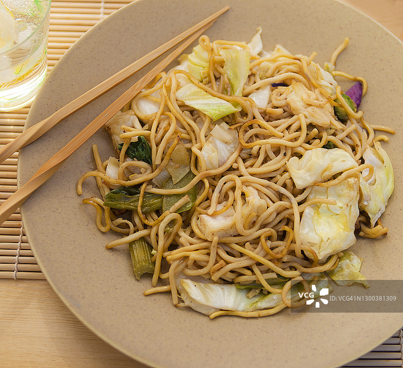 棕色盘子里的素炒面特写，配有面包、筷子和柠檬水图片素材
