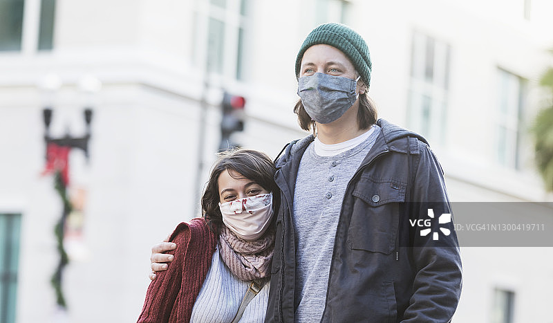 年轻情侣戴着口罩在城市里散步图片素材