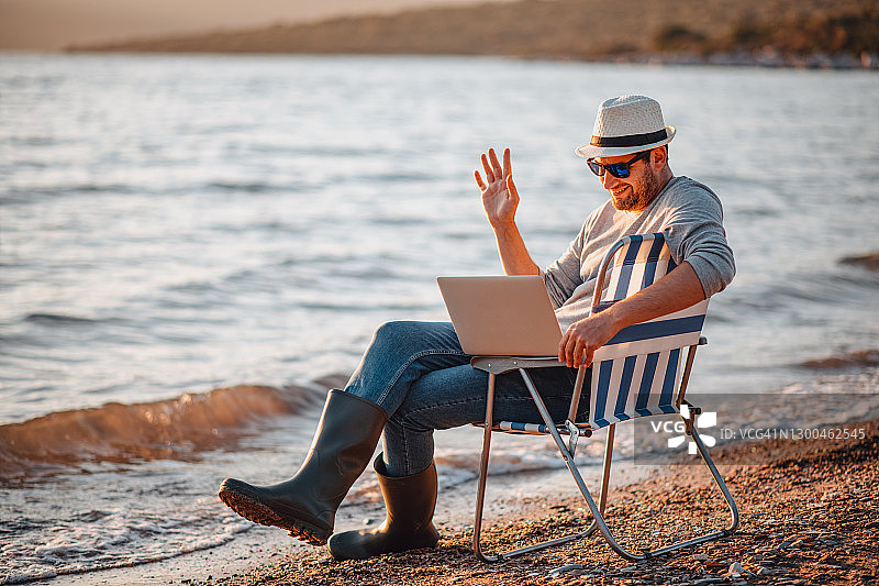 年轻男子在海滩上用笔记本电脑进行视频通话图片素材