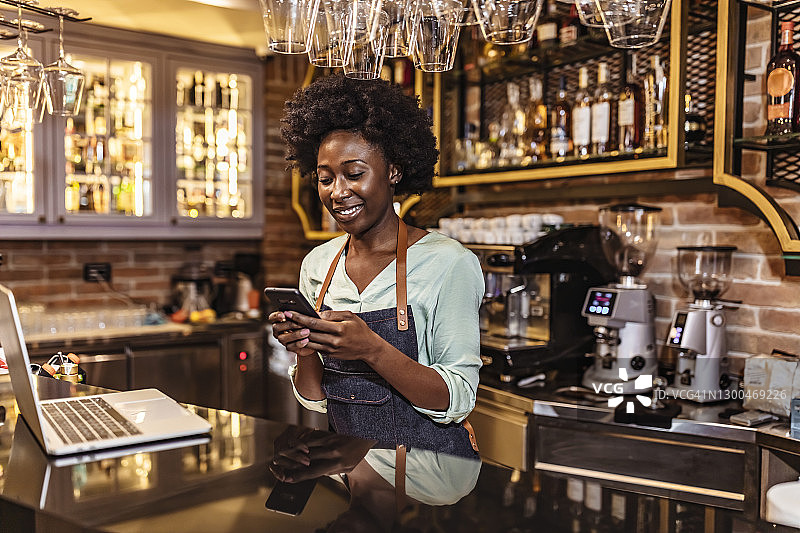 站在咖啡店里使用智能手机的女咖啡师图片素材