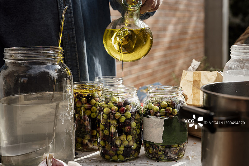 年长的男人在桌子上将橄榄油倒入玻璃罐中图片素材