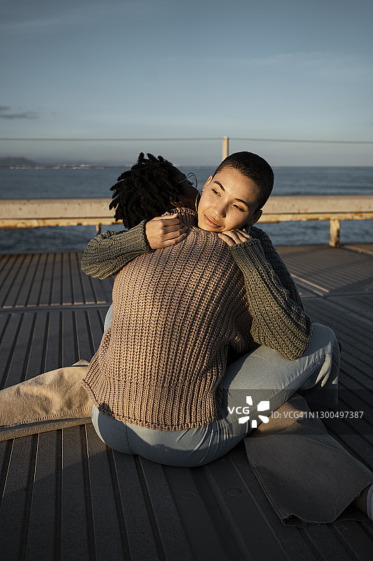 夕阳下坐在人行道上拥抱的年轻女性图片素材