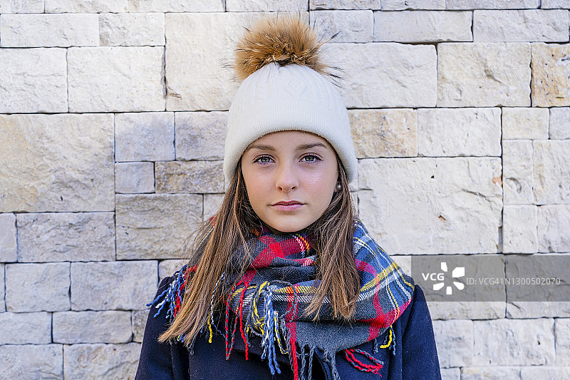 自信的青少年女孩穿着保暖的衣服倚靠在家中的砖墙上图片素材