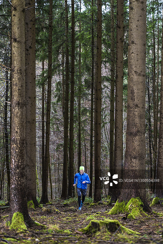 穿着蓝色夹克的男人在森林里跑步图片素材