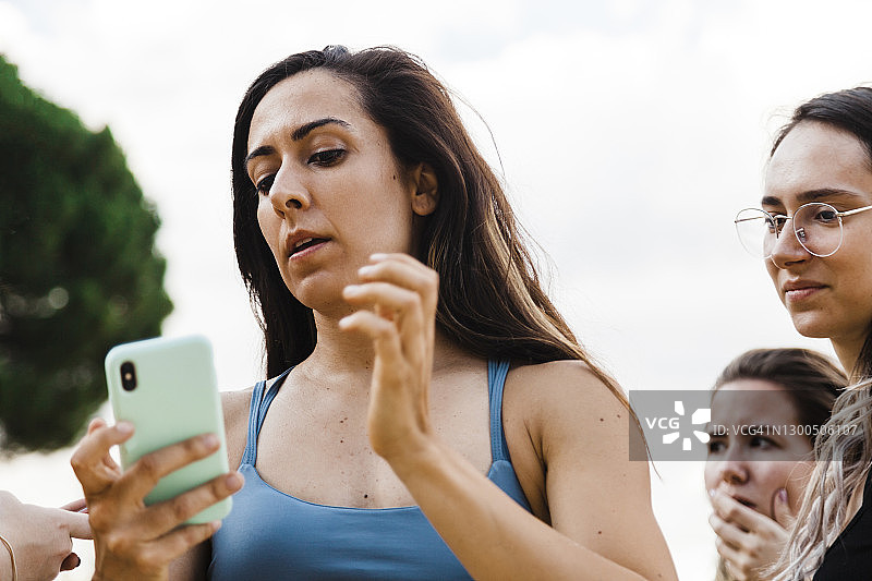 与朋友在天空背景下看手机的女人图片素材