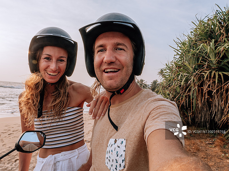 情侣在海滩边骑着摩托车在日落时自拍图片素材