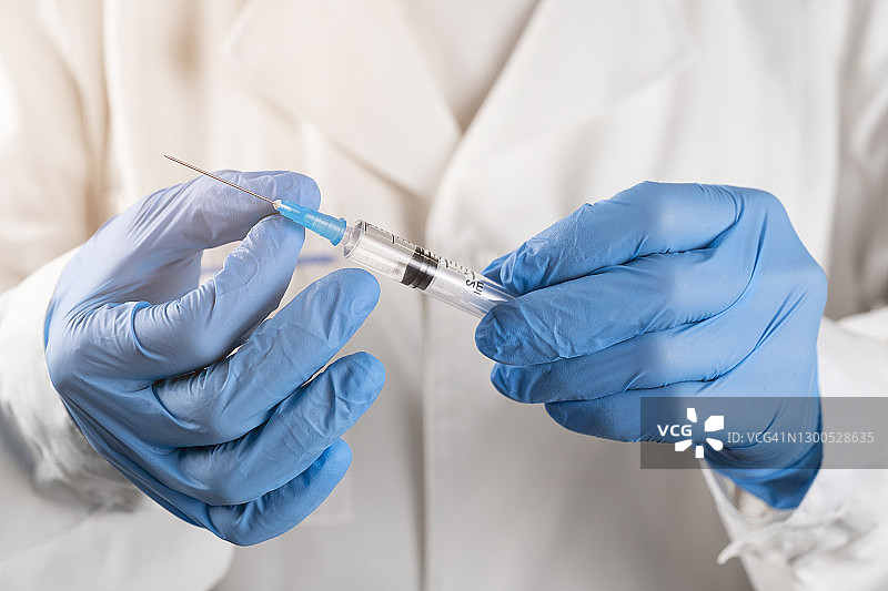 穿白大褂戴防护手套的医生拿着装有新冠疫苗的注射器图片素材