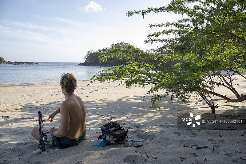 年轻男子在清晨的白色沙滩上放松，手持鱼叉枪图片素材