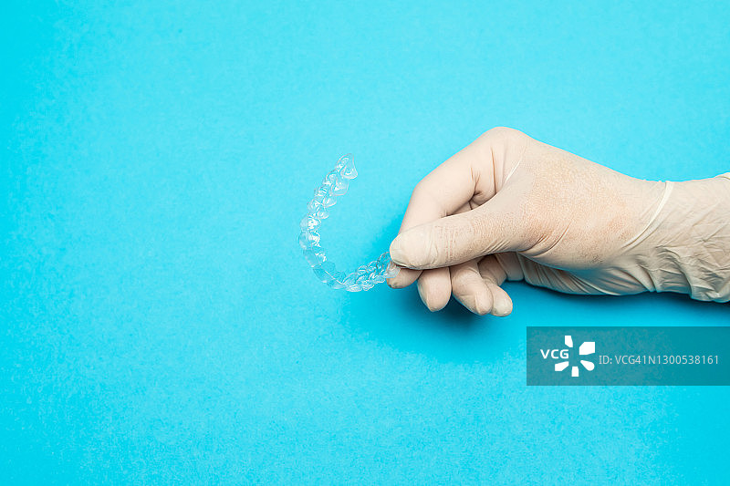 牙医戴着白色乳胶手套，在浅蓝色背景下拿着透明的牙齿矫正器，牙齿正畸概念图片素材