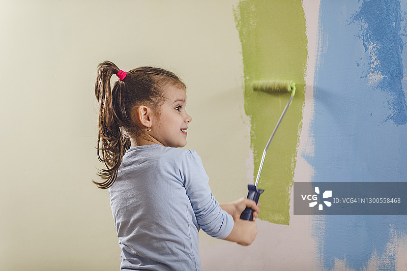 快乐的小女孩把墙壁涂成绿色图片素材