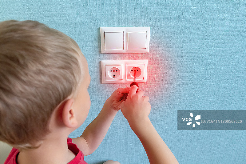 男孩用螺丝刀触摸墙上的电源插座，有触电和家庭事故的风险图片素材