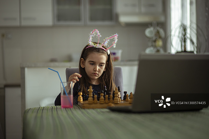 可爱小女孩与亲戚或叔叔下棋，通过笔记本电脑进行视频通话图片素材
