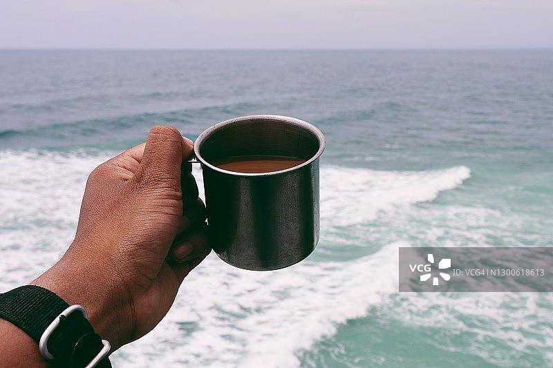 男人手握咖啡杯的特写，背景是海图片素材
