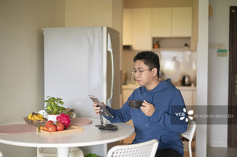 在家中餐桌旁，使用平板电脑查看邮件的华裔男子图片素材