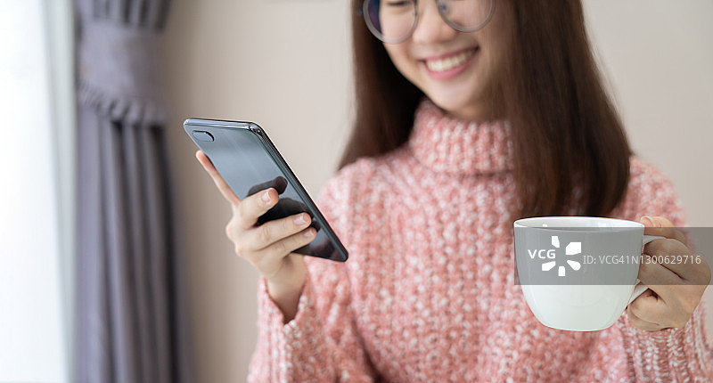 女孩坐在沙发上，一边喝咖啡一边用手机看视频，和朋友们聊天图片素材