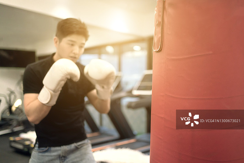 在健身房用沙袋练习拳击的亚洲男人图片素材