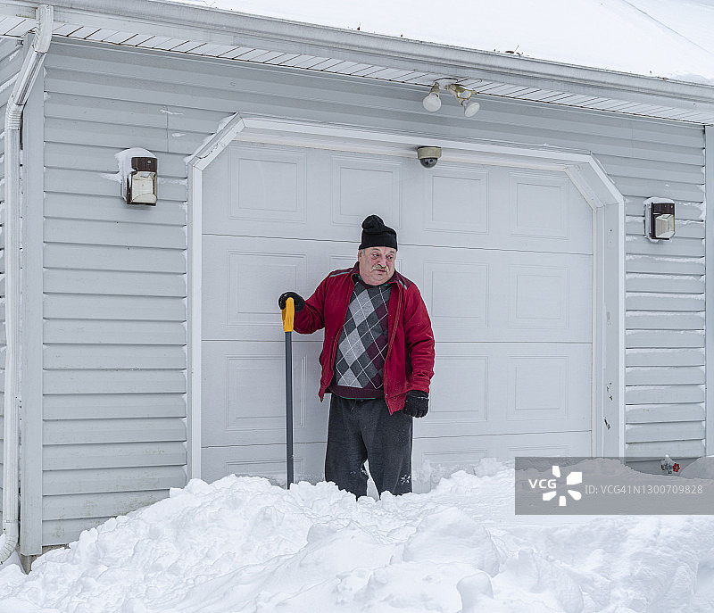 疲惫的老年男人拿着铲子在车库前清理积雪时休息图片素材