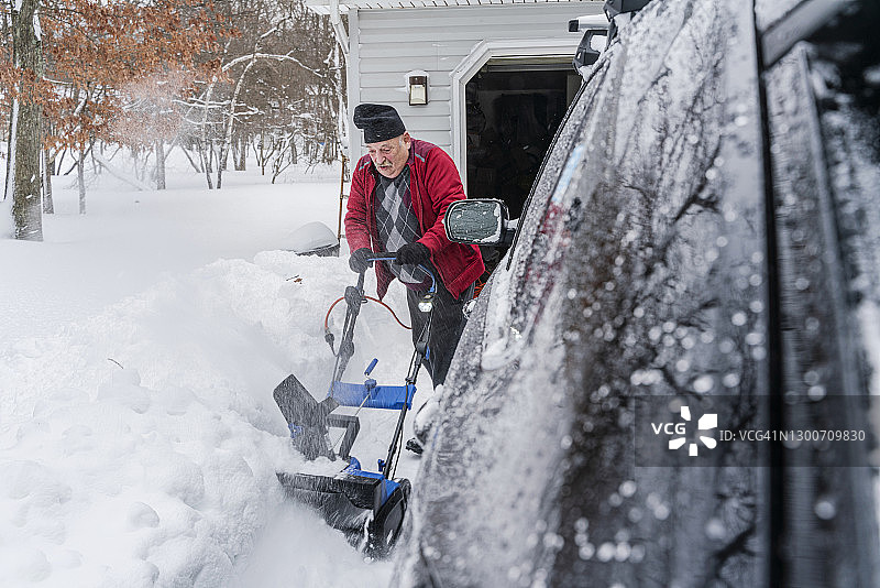 年长的男人用扬雪机清理车库前的积雪图片素材