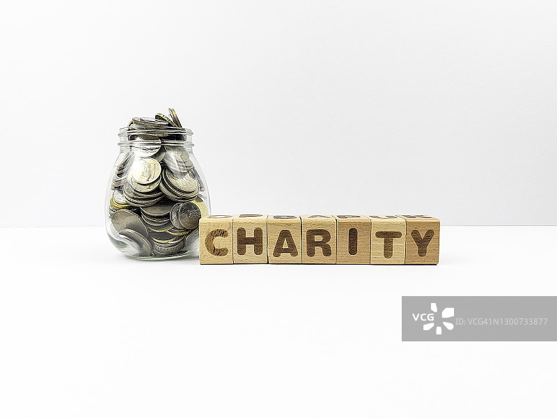 魔方形状木块玩具上的慈善文字或单词，罐子里装满了硬币。储蓄、基金和金融概念，白色背景图片素材